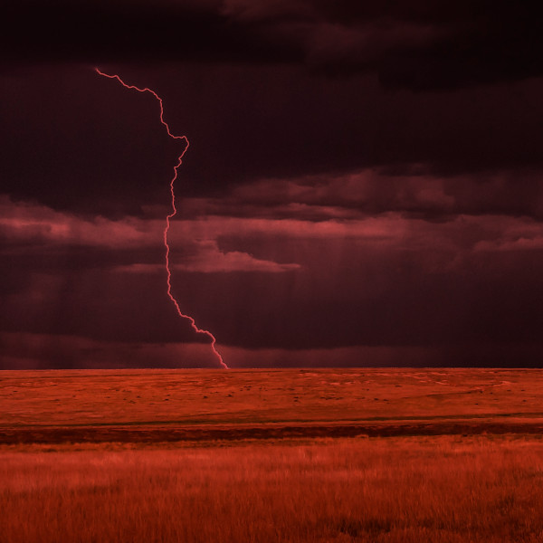 lightning striking a flat, grassy landscape with no trees, the color of the photo shifted to a dark red